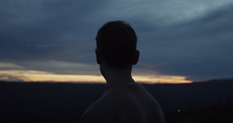 Close up view of the back of the white male at the summit of the mountain looking around in the dark towards the sunrise or sunset on Mount Batur in Bali, Indonesia
