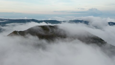 Slow aerial shot of thick fog clouds surrounding a Batur mountain in a tropical climate on the island of Bali