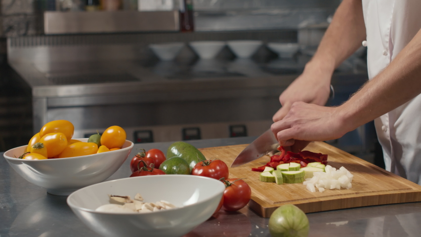 Midsection slow-motion close-up of unrecognizable male chef cutting fresh vegetables on wooden board cooking at restaurant kitchen