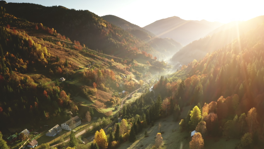 Aerial mist over mountain village at sun day. Autumn nobody nature landscape. Cottages on mount hills. Green pine trees forest at rural road in fog. Unknown misty Carpathian ridges, Ukraine, Europe