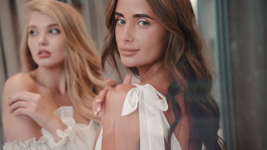 Two models look at camera and wear white wedding dress. Elegant young female friends pose. Blonde | Shutterstock HD Video #1066927009