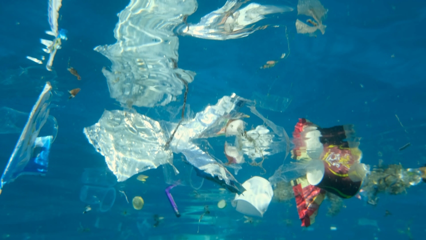 Closeup of plastic pollution of the Ocean. A lot of plastic debris drifting under water surface reflecting from the water surface. Plastic bags and cups swims on the blue water Royalty-Free Stock Footage #1066927516