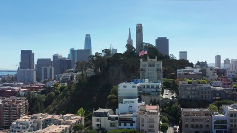Beautiful San Francisco background on sunny day. Famous Coit tower landmark with modern downtown skyscrapers on background. American flag proudly waving on hill with colorful historic victorian homes