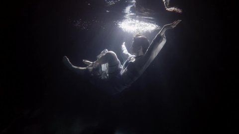 silhouette of sinking woman underwater, floating and diving under surface of dark pool