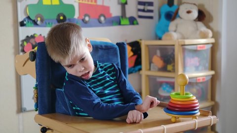 Sensory Activities for kids with disabilities. Preschool Activities for Children with Special Needs. Boy with with Cerebral Palsy in special chair play and smile at home
