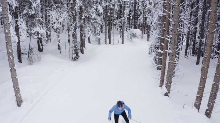 Aerial shot of Professional athlethe cross country skier running on skis trough the frozen forest covered in snow
