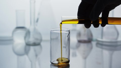 Pouring essential oil from a test tube into a flask in the laboratory. Glass flasks in the laboratory under backlit. Study of the beneficial properties of essential oils. Natural cosmetics production.