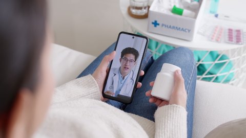 Over shoulder view of young asia woman talk to doctor on cellphone videocall conference medical app in telehealth telemedicine online service hospital quarantine social distance at home concept.