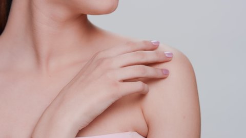 Close-up beauty portrait of young Caucasian woman softly touches her perfect skin strokes her fingers along clavicles, up to her shoulder and looks at camera | Skin care products commercial concept