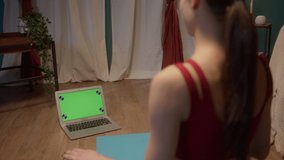 Fit young woman doing yoga stretching exercises with laptop online at home. Self-isolation during coronavirus lockdown, sport remote education on the Internet. Healthy lifestyle concept, home gym.