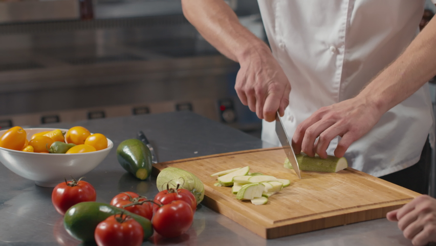 Midsection close up of unrecognizable professional chef teaching young female cook to cut vegetables properly using chef knife and wooden cutting board Royalty-Free Stock Footage #1066943164