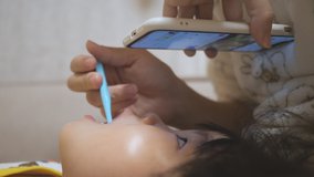 Asian toddler girl has brush teeth while watching an animated video on smartphone device before going to bed. 2 to 3 years old preschool child with head resting on mom's lap. Parenting and childcare