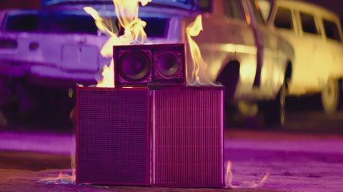 Scene of burning speaker in abandoned garage . Purple and blue lights . Speaker is burning on the concrete floor in the street . Fire burning in slow motion . Vintage and retro style . 