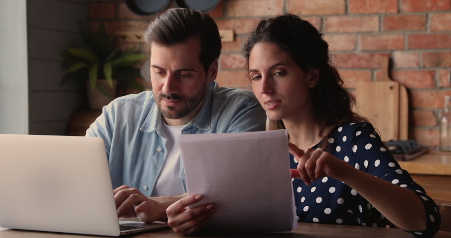 Young married couple holding correspondence papers, do paperwork analysis, reading document, discuss agreement details, learn insurance cover contract terms conditions sit at table in kitchen at home Royalty-Free Stock Footage #1066944736