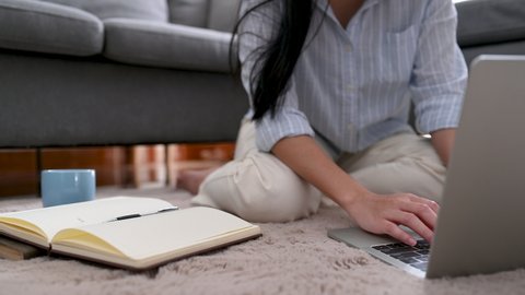 Young asian businesswoman is searching for information on a laptop and she took notes on a notebook and she was sitting on the rug in the living room at home.Business woman and working concept.