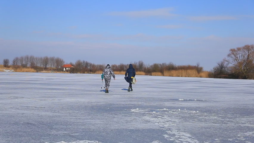 Two fishermen pass through a snow-covered winter lake in search of fish