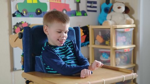 Activities for kids with disabilities. Preschool Activities for Children with Special Needs. Mom is playing with Boy with Cerebral Palsy in special chair at home.