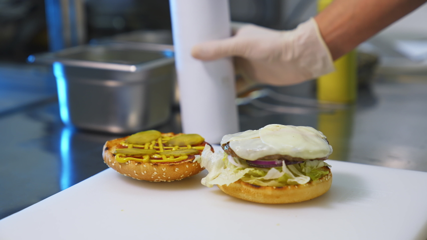 Making hamburger in fast food restaurant. Hand of man smears sauce on a burger and covers with fried bread. Close-up.Tasty burgery ready to eat.