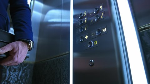 Businessman in lift. Male's hand pressing button to start moving inside the elevator. Man touches elevator button in hotel or high-rise building.