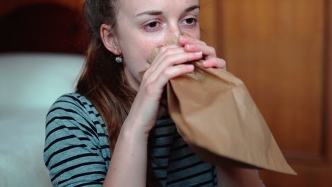 Shocked woman breathing into brown paper bag to calm down, frightened female having suddenly panic attack. Anxiety, mental disorder, epilepsy and asthma concept