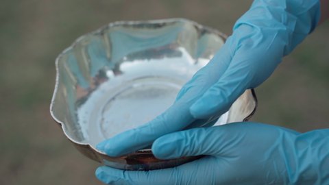 Process of cleaning antique silver plate with shiny polish, collector in protective gloves rubbing silver bowl surface for rust cleaning. Antioxidant action for silver items, vintage utensils