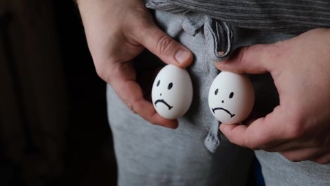Urology, male sexual problems concept. Decreased testosterone, sexual activity. A man holds chicken eggs with sad emoticons near the groin.