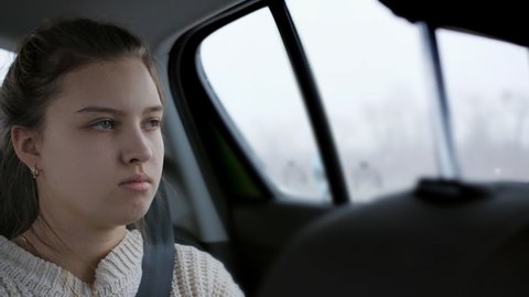 A sad girl in the back seat of a car looks out the window while traveling by car.