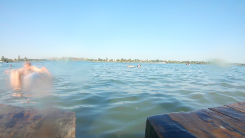 couple jumping from wooden pier into water in slow motion. copy space. summer vacation