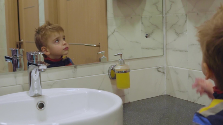 Little boy wipes his face with paper towels while looking at himself in the mirror in the bathroom. Independent child