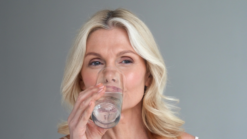 Happy healthy thirsty smiling fit middle aged mature 50s woman holding glass drinking clean filtered fresh mineral water looking at camera. Body and aging skin beauty hydration, self care concept. Royalty-Free Stock Footage #1066964743