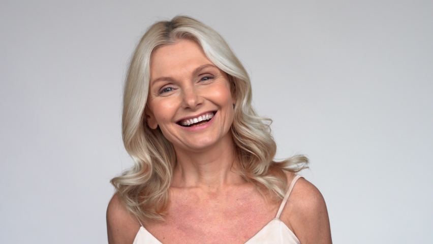 Happy smiling beautiful 50s middle aged mature woman looking at camera, laughing on white background. Anti age face beauty, skin and body care, wellness and self care concept. Close up portrait. Royalty-Free Stock Footage #1066964761