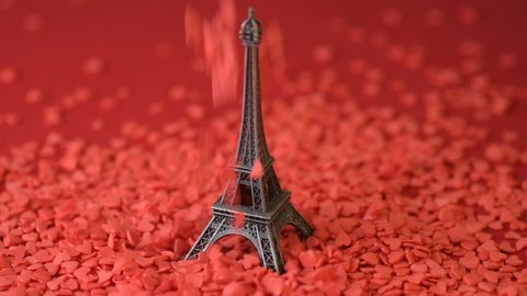 Eiffel tower statuette on red background red scarlet heart shaped sugar confetti fall down scatter slow motion. France, romantic love, Saint Valentine's Day preparation design concept