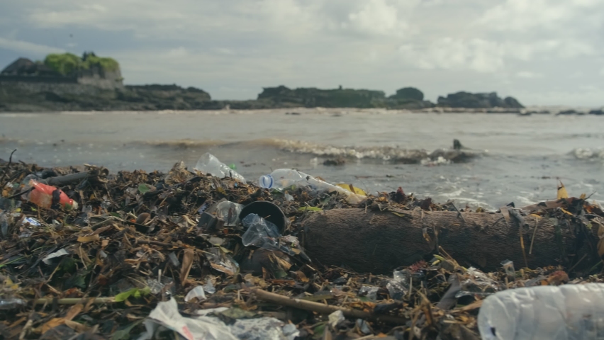 Spilled garbage on ocean beach coast Bali island empty used dirty plastic bottles and other chemical waste. Dirty sea sandy shore environmental pollution ecological problem, moving waves in backdrop Royalty-Free Stock Footage #1066978339