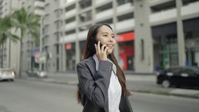 Video Slow-motion. Asian woman, beautiful businesswoman, white skin, in a black suit, talking on a smartphone. On the side of the street in the city