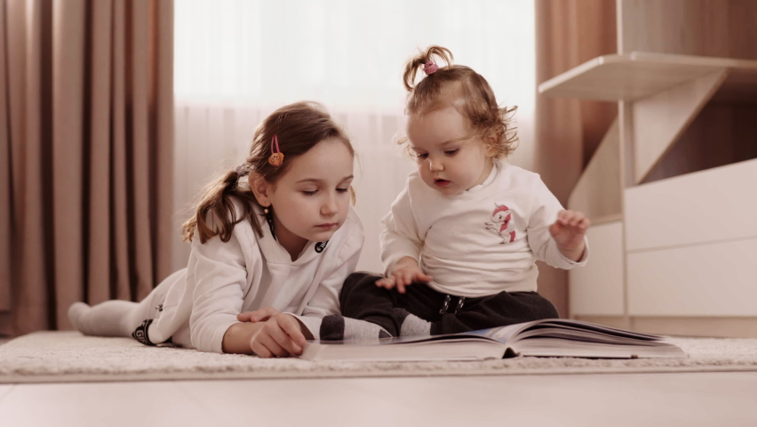 Two sisters flip through a book on the carpet in the middle of the room. High quality 4k footage | Shutterstock HD Video #1066982575