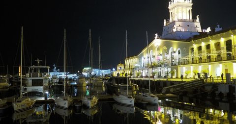SOCHI, RUSSIA - March 03, 2020. Yachts moored at pier. Famous building of Sochi seaport at night.