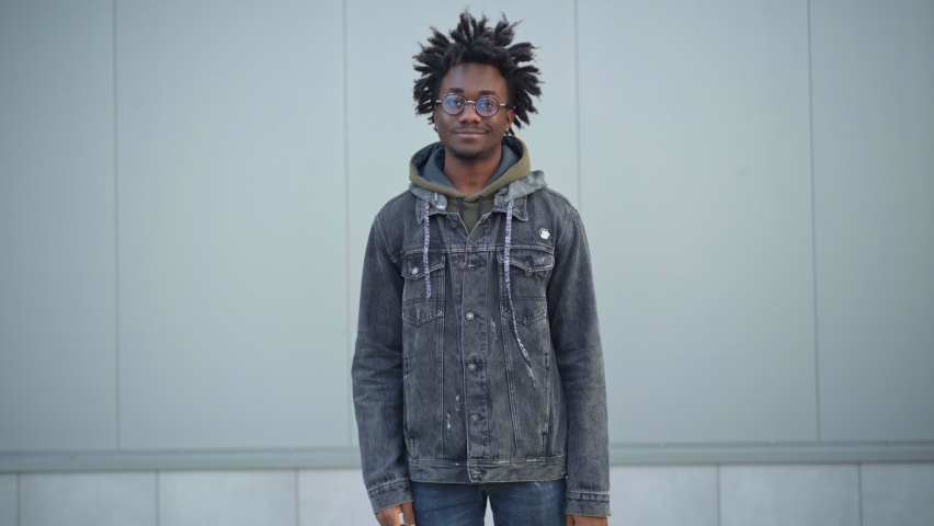 Cheerful African American young man showing thumb up raising yellow insulated food delivery bag looking at camera. Portrait of smiling courier posing in urban city outdoors. Service concept.