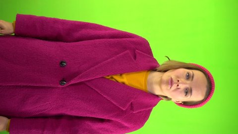 Vertical Footage. Displeased Woman in red coat and hat Shows Thumbs Down. Sad Hand Gesture. Emotions of failure. Serious facial expression. Green background, studio video, 4K, chromakey.