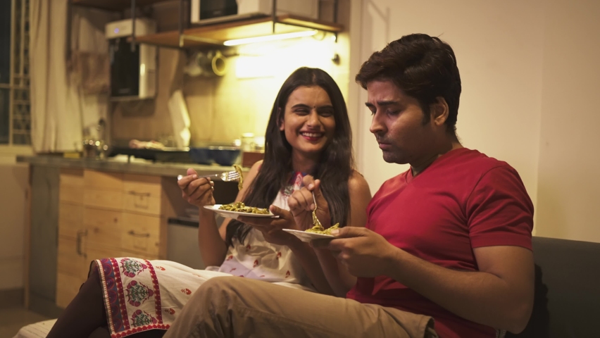 A happy and attractive young Indian couple sitting on a couch and having home-cooked food together in an apartment, also enjoying a evening meal  Royalty-Free Stock Footage #1066996942