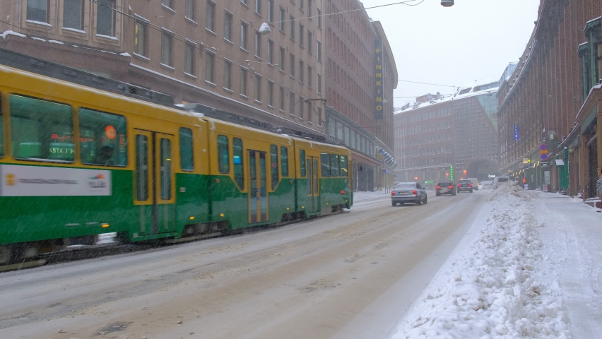 Helsinki, Finland - January 12, 2021: Kaivokatu street during the strong snowstorm. Tram, cars, bus are moving on the snow-covered street.