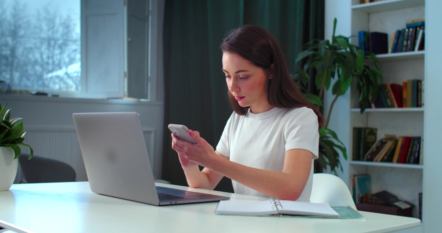 Young female student prepares homework using mobile phone laptop indoors slow motion. Casual woman searching information for project in smartphone. Freelance home education coronavirus quarantine  Royalty-Free Stock Footage #1067009938