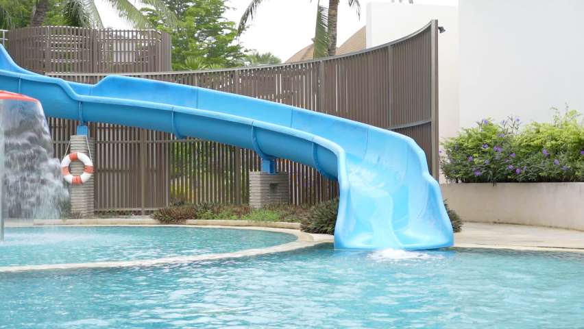 Asian child cute or kid girl enjoy with happy fun playing water slider on swimming pool or waterpark for fresh relax with exercise activity on summer holiday travel and family vacation on slow motion