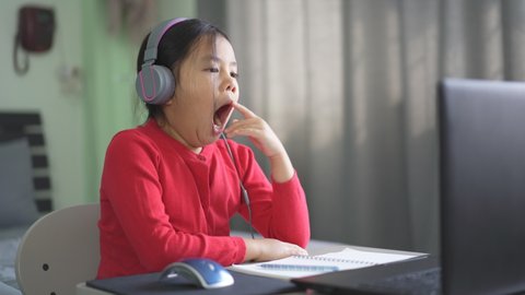 Asian child or kid girl e-learning on computer notebook to wearing headphone and sleepy yawn or bored to video call communication by study online or people learn from home by laptop to back to school