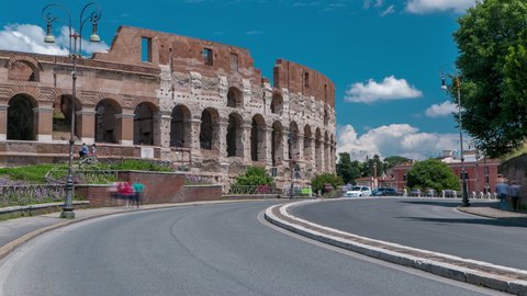 Many tourists visiting The Colosseum or Coliseum timelapse, also known as the Flavian Amphitheatre in Rome, Italy. Traffic on the road and cloudy blue sky