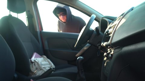 A Thief in a Black Hoodie and Black Glasses Steals a Women's Wallet from an Open Car during the day. Blurred Video.
