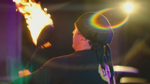 Adult man with bandanna dressed in black performing cool and dangerous fire show and doing many tricks with fire burning iron chain at night. Abandoned dark building. Slow motion shot. 
