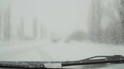Highway with police car with siren and blinking blue lights in winter from windscreen with drops of water. Automobile in snowy frozen road