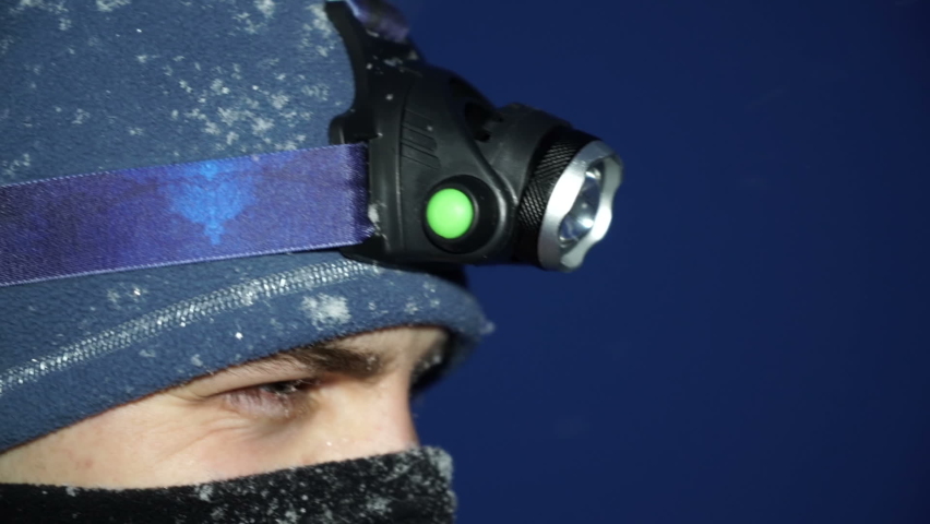 Man at snowy night turning on Headlamp