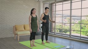 Happy asian couple exercise together by watching workout video in living room home. Sporty woman and man smile and make exercise on yoga mat indoors daily routine. Healthcare and home fitness concept.