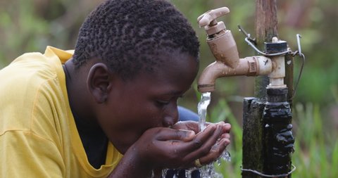 Close-up portrait of a young black African boy sitting drinking water at a communal water point. Water crisis. Poverty. Climate change. Global warming. Drought.Inequality